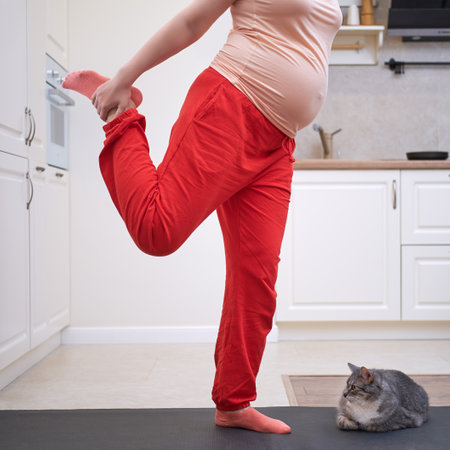 A pregnant woman is engaged in fitness in the home kitchen and does foot and knee stretchingの写真素材