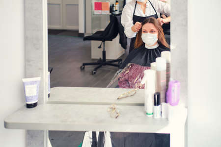 A woman gets her hair cut in a barber shop in a medical face maskの写真素材