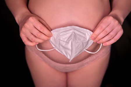 Pregnant woman on black background with medical mask n95 ffp2. Concept of protectionの写真素材