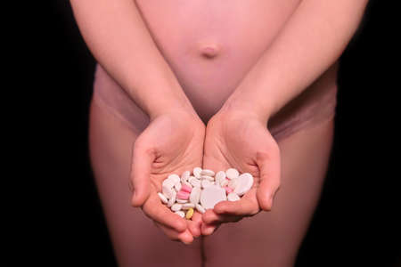 Pregnant naked belly and a handful of white pills. Pregnancy drug problem conceptの写真素材