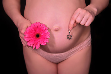 Pregnant naked belly and hand with the symbol of Judaism faith and red gerbera flower, six-pointed...