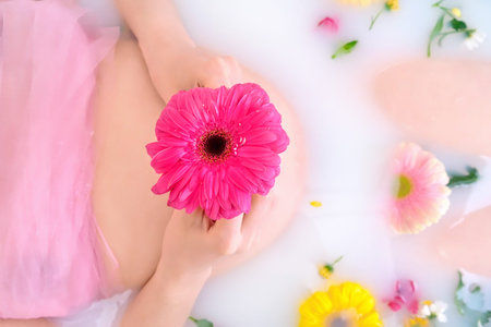 Red gerbera flower on the belly of a pregnant woman in a bath with water