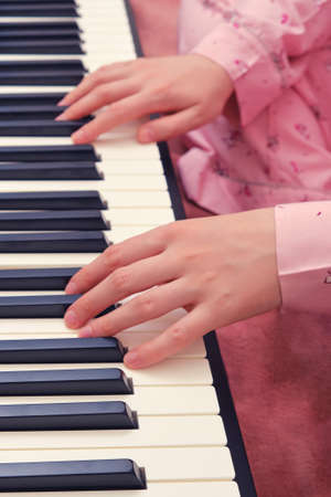A woman is engaged in music sitting at a synthesizer on a home bed, hands close-upの写真素材