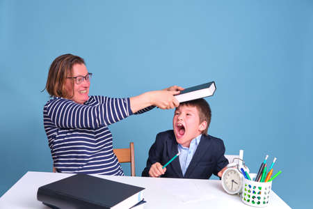 Angry teacher hits junior boy with book at desk, learning problems in primary schoolの写真素材