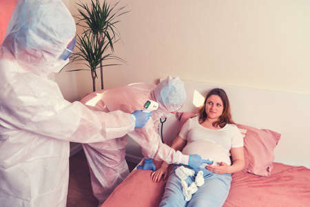 A pregnant woman and paramedics in protective uniforms measure the temperature with a thermometerの写真素材