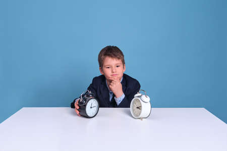 Schoolboy elementary school boy sits thoughtfully at the table, blue backgroundの写真素材