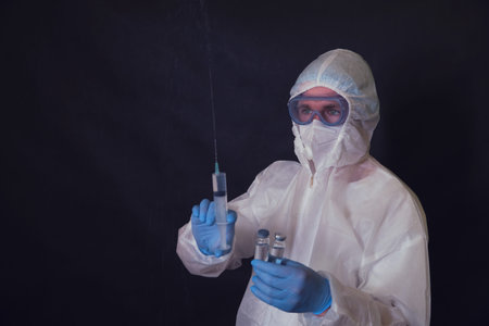 A doctor in a covid protective suit with a syringe and ampoules in his handsの写真素材
