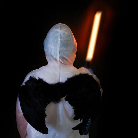 Male doctor with a fiery sword and black wings in a protective uniform on a dark backgroundの写真素材