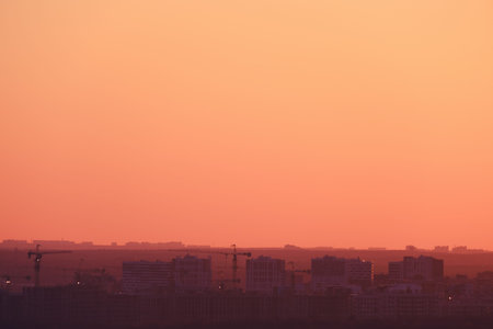 Buildings in a city under construction against the background of an orange sunset sky, copy spaceの写真素材