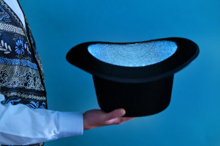 Hat in the hands of a magician on a blue background, close up