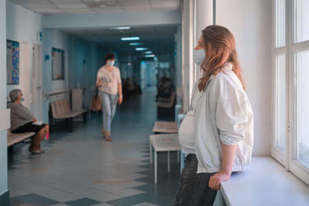 Pregnant woman in the lobby of the clinic with a medical mask on her faceの写真素材