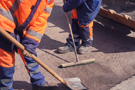Road workers in uniform with shovels and mekla change the asphaltの写真素材