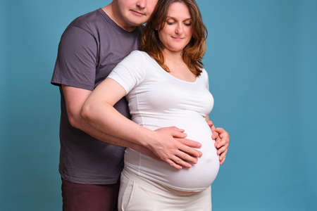 Man hands on pregnant woman's tummy, studio shot on blue backgroundの写真素材