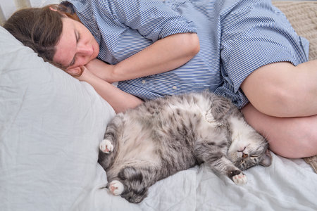 A pregnant woman and a gray cat sleep on a bed during the dayの写真素材