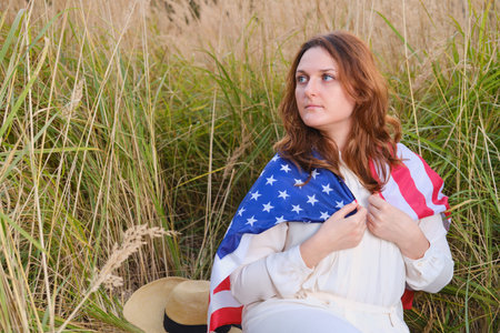 Happy woman wrapped up in the US flag in the autumn nature