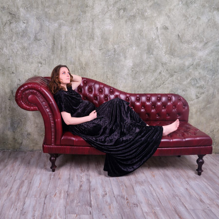 Red sofa in the studio and a pregnant woman in a long black dress