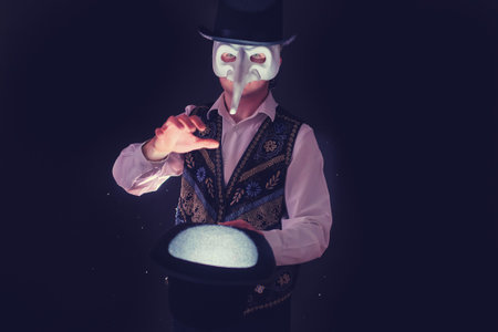 A magician wearing a plague doctor mask on his face with a hat in his handsの写真素材