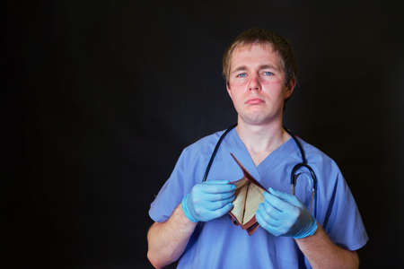 A doctor in a blue uniform with an empty wallet without money on a black backgroundの写真素材