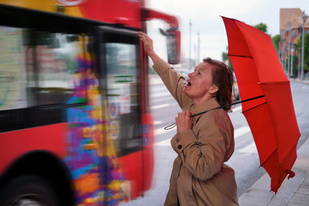 Adult woman with a red umbrella in the rain at the tourist busの写真素材
