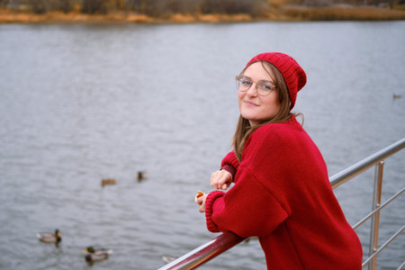 Smiling woman feeding ducks at autumn lake, outdoor