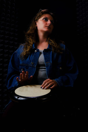 Playing on ethnic African percussion instrument Darbuka, horizontal photo. A young woman plays a drum djembe sitting on the floor in a recording Studio.の写真素材
