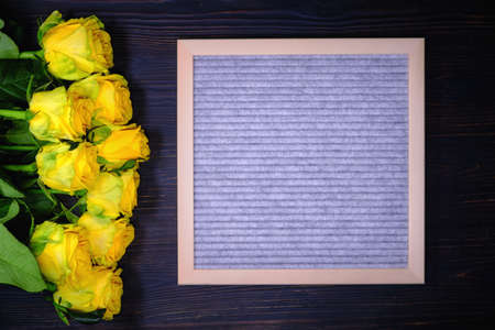 Yellow roses on a dark wooden background, copy space. A bouquet of beautiful flowers and a writing Board. A place to write a text about love.の写真素材
