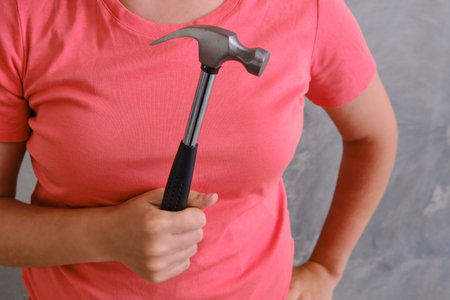 Woman in red holding an iron hammer. Builder on the background of a built house. Repair yourself in...
