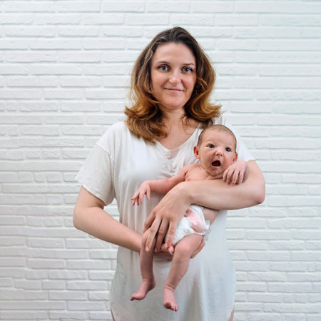 A happy adult woman holds a newborn baby boy against the background of a white brick wall