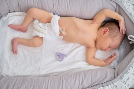 A baby boy sleeps in a cocoon on a cot. A newborn baby in a diaper is lying naked on the bed
