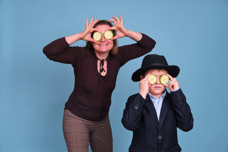 An adult woman and a funny boy hold two circles of zucchini in place of the eyes, blue studio...