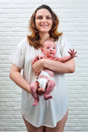 A happy adult woman holds a newborn baby boy against the background of a white brick wall