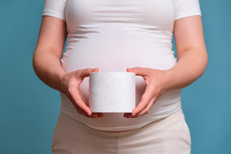 Toilet paper in hands of pregnant woman, studio shot on blue background