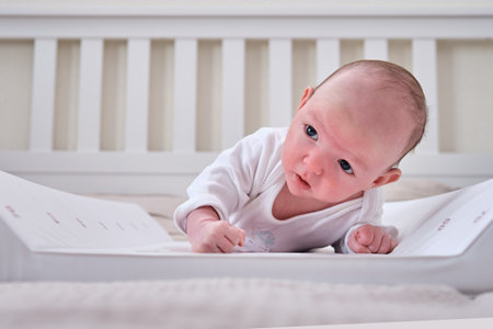 A baby aged 1 month learns to keep his head lying on his stomach. Caucasian boy child in a home white bedroomの写真素材