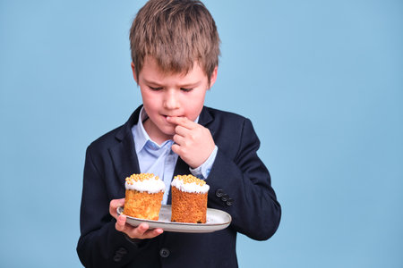 A boy with an Easter cake in his hands, copy space on a blue studio backgroundの写真素材