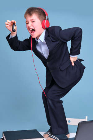 A boy in a school suit with headphones on distance learning, copy space on a blue studio backgroundの写真素材