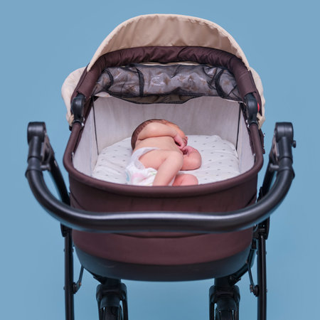 Baby boy in a stroller on a blue background. A naked child in only diapers is lying in a stroller,...