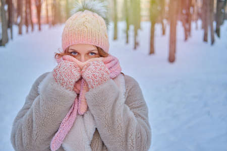 A smiling woman wraps herself in clothes warming up in a winter forest with trees in the snowの写真素材