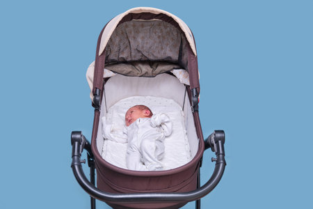 Baby boy in a stroller on a blue background. A child in white clothes in only diapers is lying in a stroller, studio shotの写真素材