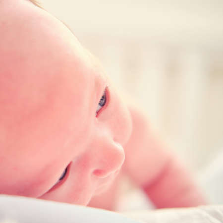 A baby aged 1 month learns to keep his head lying on his stomach. Caucasian boy child in a home white bedroomの写真素材