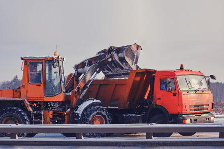 Snow removal in winter from roads with an excavator and a truckの写真素材