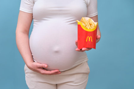 Pregnant woman with French fries from McDonald on blue background - Moscow, Russia, June 08, 2021のeditorial素材