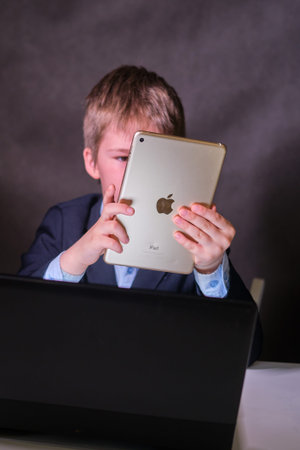 A happy boy in a school suit with a digital tablet in his hands, copy space on a dark studio...