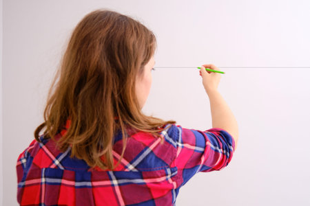 A female designer draws a line on a white wall. Hand draws the future arrangement of the room with a pencilの写真素材