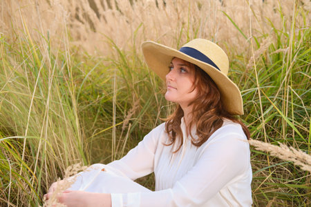 A happy woman with a smile on her face sits on the autumn grass in a field