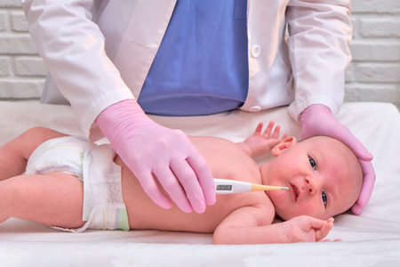 Doctor checks the temperature of the newborn baby with a thermometer. A nurse in uniform measures...