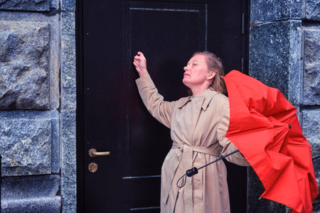 An adult woman knocks on the door of an old house in alarmの写真素材