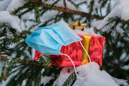 A gift in a red box and a medical face mask at the Christmas tree in winter nature on New Year Eveの写真素材