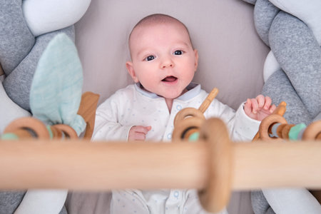 Smiling infant baby boy playing with a wooden mobile suspended above the crib. Happy child playing...