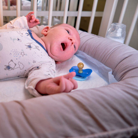 Portrait of a baby boy aged one month yawning in a crib. Caucasian sleepy child in the children...