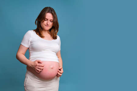 Portrait of a pregnant woman scratching her stomach, blue backgroundの写真素材